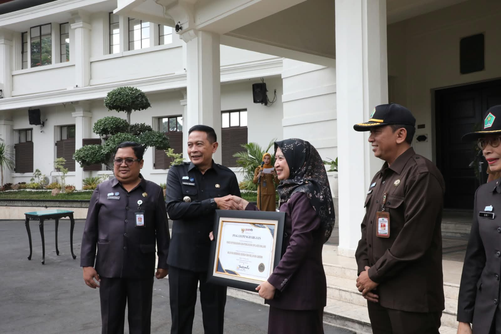 Wali Kota Malang, Dr. Ir. Wahyu Hidayat, M.M. menyerahkan penghargaan predikat Wilayah Birokrasi Bersih dan Melayani (WBBM) dari Kementerian Pendayagunaan Aparatur Negara dan Reformasi Birokrasi (PANRB) kepada Kepala Dispendukcapil Kota Malang, Ir. Dahliana Lusi Ratnasari, M.M.